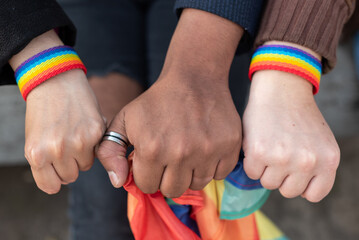Close up of three hands with   LGBTQ rainbow wristband and holding a Rainbow flag, concept of gay...