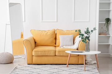 Interior of light living room with yellow sofa and eucalyptus in vase