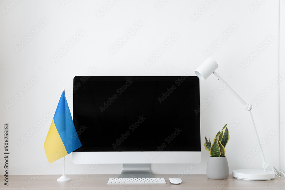 Wall mural Modern workplace with computer, flag of Ukraine, houseplant and lamp near light wall