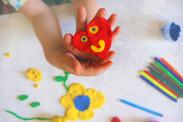 Hands of little girl making funny heart from colorful clay dough, plasticine, Home Education game...