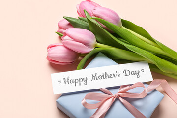 Paper with text HAPPY MOTHER'S DAY, tulips and gift box on pink background, closeup
