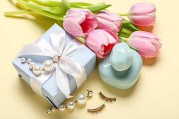 Bouquet of pink tulips, gift box and female accessories on yellow background, closeup