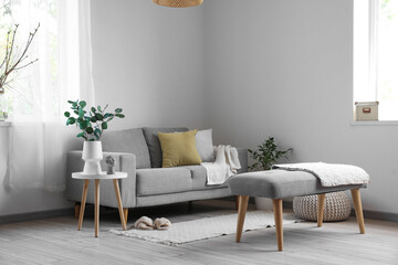 Interior of light living room with soft bench, sofa and houseplants