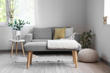 Interior of light living room with soft bench, sofa and houseplants