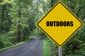 Outdoors sign in woods with road into the forest.