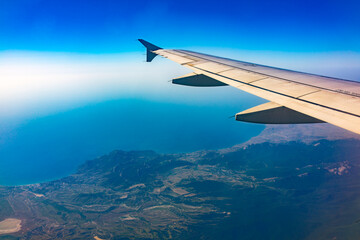 Fototapeta premium View from the airplane window at a beautiful blue clear sky, earth, sea and the airplane wing