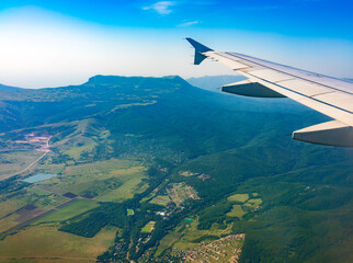 View of airplane wing, blue skies and green land during landing. Airplane window view.