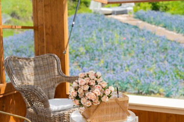 Cozy wooden cottage with picnic rattan basket with flowers bouquet with table and chairs overlooking blue flower field from the window