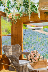 Cozy wooden cottage with picnic basket with flowers bouquet with rattan table and chairs overlooking blue flower field from the window