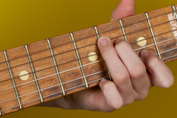 Pinch a chord on the guitar neck with your fingers on a yellow background