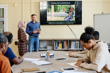Horizontal shot of multi-ethnic group of migrants attending English language classes doing tasks...