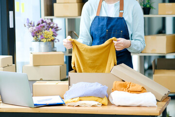 Asian female clothes shop owner folding a t-shirt and packing in a cardboard parcel box..