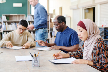 Group of multi-ethnic immigrant students sitting at table in library working on English language test