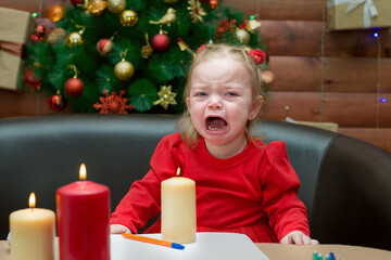 A little girl in a red dress on the background decorated Christmas tree burst into tears and calls...