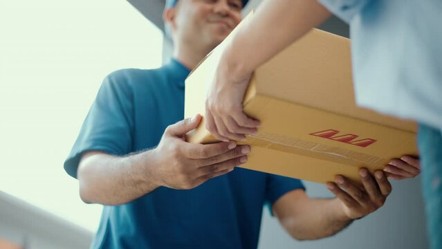 Close up parcel in hand of blue uniform delivery man to customer front of the house from shopping online with good service. Courier man delivering a cardboard box postal package to destination.