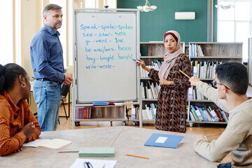 Group of multi-ethnic immigrant students learning English language at school doing task with...