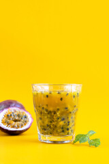 A glass of passion fruit juice with mint and passion fruit on a yellow background, space for text. A glass of freshly squeezed tropical fruit juice.
