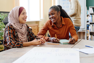 Young Black and Middle Eastern women having fun chatting about something during English lesson for immigrants - obrazy, fototapety, plakaty