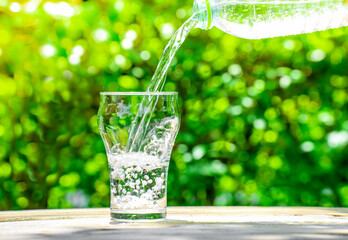 Pour water from a plastic bottle into a glass. The background of the plants in the garden.