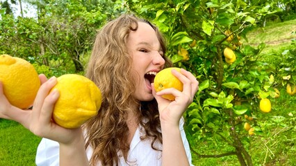 a teenage girl stands near a lemon tree and rejoices in a lemon, she sniffs them, hugs, examines. High quality photo