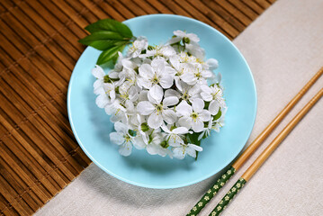 Spring composition. Round turquoise plate with white cherry flowers. Bamboo mat, chopsticks. Easy food concept, zero calorie, top view.