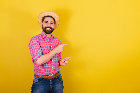 Bearded man wearing typical clothes for party Junina. showing with fingers, to the side, negative advertising and text space. For the Arraia Party
