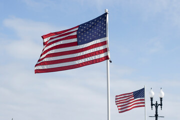 Waving American flags in the wind against clouds and blue sky on a sunny day.