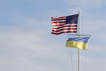 Waving American and Ukrainian flags on a flagpole against clouds and blue sky, showing American support for Ukraine amid the Russia-Ukraine war.