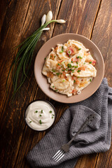Potato dumplings with sour cream on the wooden table. Traditional ukrainian food. Varenyky, vareniki, pierogi, pyrohy - dumplings with filling.