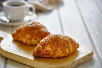 A crispy croissant with almond filling and hot black coffee on a wooden board on a light concrete table.