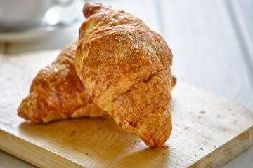 A crispy croissant with almond filling and hot black coffee on a wooden board on a light concrete table.