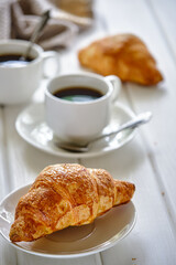 A crispy croissant with almond filling and hot black coffee on a wooden board on a light concrete table.