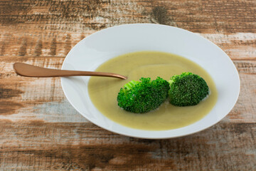 Cream of broccoli soup with two florets of steamed broccoli in white soup bowl with copper colored spoon