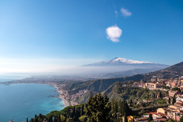 Panoramic view on snow capped Mount Etna volcano and Mediterranean coastline on sunny day seen from coastal hilltop town Taormina, island Sicily, Italy, Europe, EU. Vacation tourism travel destination - obrazy, fototapety, plakaty