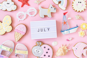 July text on lightbox and cute summer symbols on pink background. Top view, Flat lay. Creative summer concept, greeting card