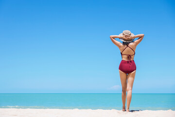 Young women in bikini and straw hat stand on tropical beach enjoying looking view of beach ocean on hot summer day. Blue sea in background. Khao Lak, Phang Nga, Thailand. Summer vacation concept