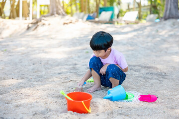 Asian boy sitting play sand with his sand toy set on enjoy tropical beach. Summer vacation concept