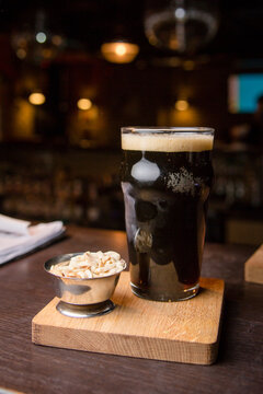 A glass of dark beer with nuts on the bar. vertical photo