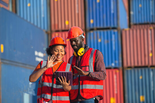 Happy African American female and male worker using tablet and greeting someone during video call in a logistic shipping cargo containers yard.