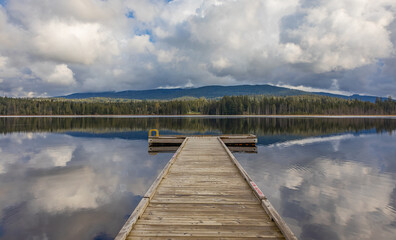 Fototapeta premium Idyllic view of a wooden pier in the lake with mountain scenery background in cloudy morning