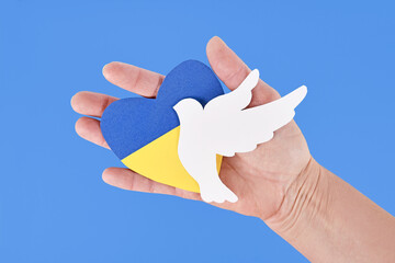 Hand holding dove of peace and heart with Ukraine flag colors blue and yellow