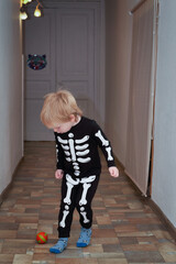A child in a skeleton costume plays football in the hallway of the house - 506778786