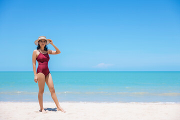 Fototapeta na wymiar Young women in bikini and straw hat stand on tropical beach enjoying looking view of beach ocean on hot summer day. Blue sea in background. Khao Lak, Phang Nga, Thailand. Summer vacation concept