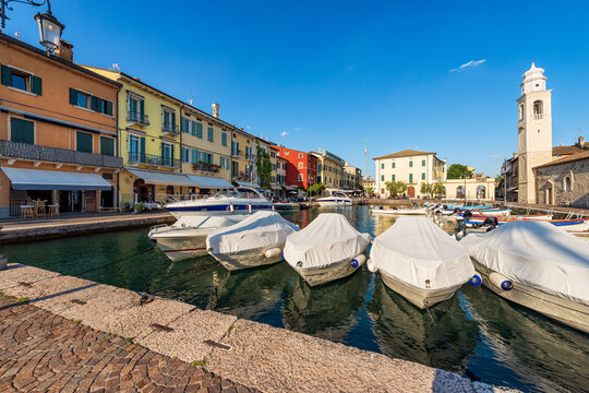 Small port of the Lazise village with moored boats. Tourist resort on the coast of Lake Garda (Lago di Garda). Verona province, Veneto, Italy, Europe. Ancient church of San Nicolò in Romanesque style.