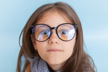 Portrait of a 7 year old girl with long hair in glasses with bulging eyes looks at the camera