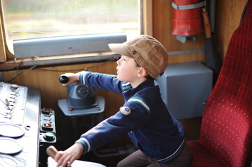 A young boy steering a locomotive and train in a driving compartment or cabin with handles and meters as a train driver, engine driver, engineman, locomotive driver, engineer, locomotive handler