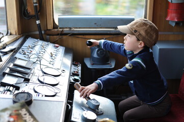 A young boy steering a locomotive and train in a driving compartment or cabin with handles and...