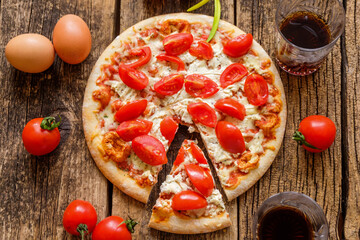 A Margarita pizza with cheese and tomatoes in the center of a wooden board near some glasses with drinks and ingredients