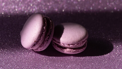 A set of two purple macaroons and a rose on sparkling purple background