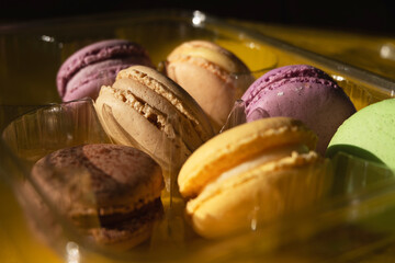 Set of multiple colorful macarons in a plastic container, yellow background and sparkles in the dark